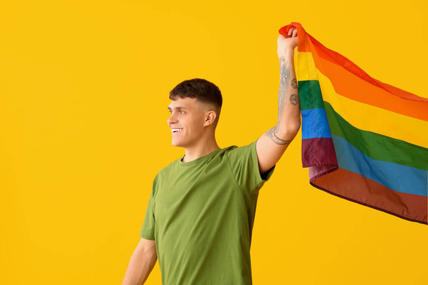 Όμορφος νεαρός ευτυχισμένος άντρας με σημαία ΛΟΑΤ σε κίτρινο φόντο - Φωτογραφία, εικόνα