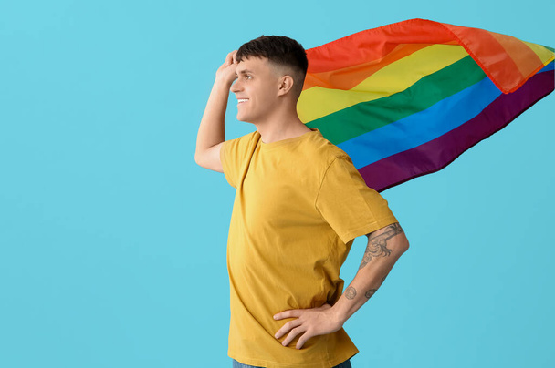 Красивий молодий щасливий чоловік з ЛГБТ прапорами на синьому фоні - Фото, зображення