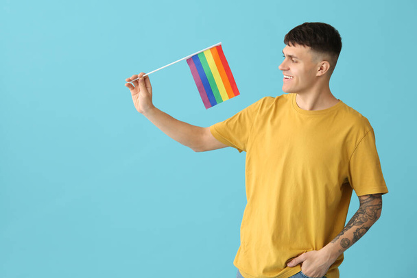Schöner junger glücklicher Mann mit LGBT-Flaggen auf blauem Hintergrund - Foto, Bild