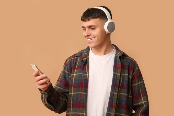 Knappe jonge gelukkig man in hoofdtelefoon met mobiele telefoon luisteren audioboek op beige achtergrond - Foto, afbeelding