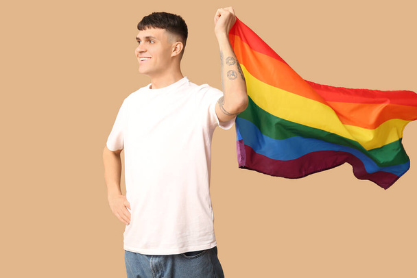 Красивый молодой счастливый человек с флагом ЛГБТ на бежевом фоне - Фото, изображение