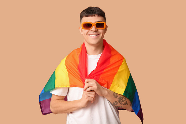 Guapo joven feliz hombre con bandera LGBT sobre fondo beige - Foto, imagen