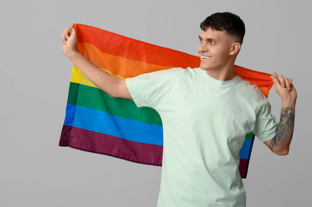 Hezký mladý šťastný muž s vlajkou LGBT na šedém pozadí - Fotografie, Obrázek