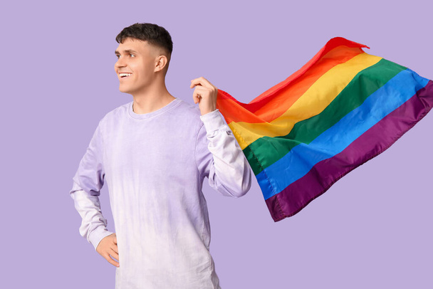 Handsome young happy man with LGBT flag on purple background - Photo, Image