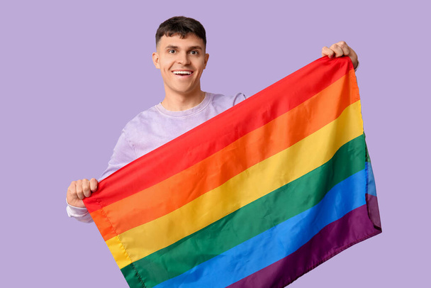 Guapo joven feliz hombre con bandera LGBT sobre fondo púrpura - Foto, imagen