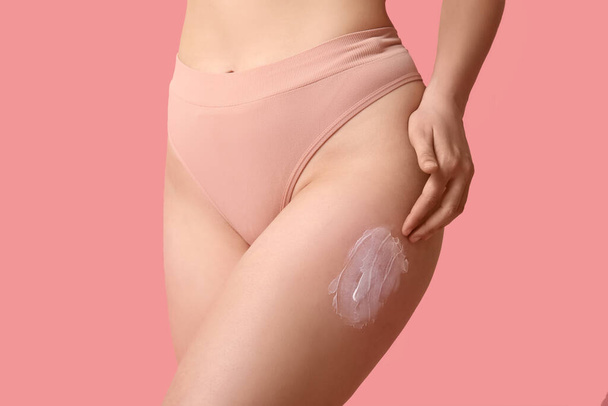 Beautiful young woman with anti-cellulite cream on pink background, closeup - Photo, Image