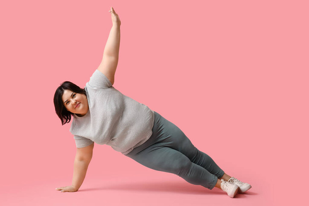 Junge übergewichtige Frauen beim Training auf rosa Hintergrund. Konzept zur Gewichtsreduktion - Foto, Bild