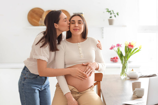 Mladé lesbičky žena líbání ji těhotná manželka v kuchyni - Fotografie, Obrázek