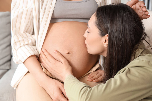 Young lesbian woman kissing her pregnant wife's belly at home, closeup - Photo, Image