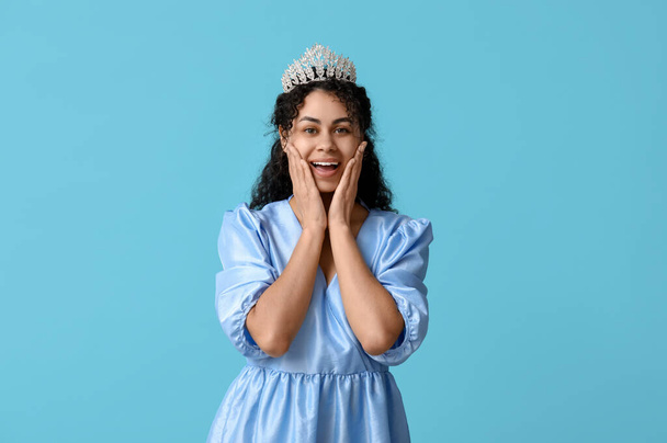 Surprised young African-American woman in beautiful tiara and stylish dress on blue background - Photo, Image