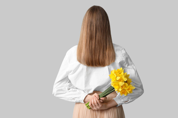 Jovem com buquê de belas flores daffodil no fundo cinza, visão traseira - Foto, Imagem