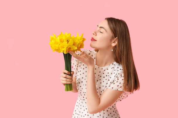 Beautiful young woman with bouquet of daffodil flowers on pink background - Photo, Image