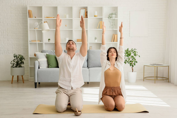 Pareja joven deportiva practicando yoga en la sala de estar ligera - Foto, Imagen