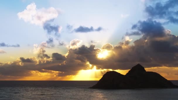 Φωτεινές χρυσές ακτίνες που λάμπουν μέσα από μπλε σύννεφα πάνω από τον ωκεανό. Δραματική φύση στα νησιά της Χαβάης. Ταξίδι περιπέτειας Oahu. Εκπληκτική ανατολή πάνω από τα νησιά Na Mokulua στην ανεμοδαρμένη ακτή του νησιού Oahu - Πλάνα, βίντεο