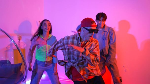 Hispanic hipster wear colorful cloth and waving to freestyle music. Professional break dancer moving to lively beat with neon light and led light with modern studio surrounded by friend. Regalement. - Photo, Image