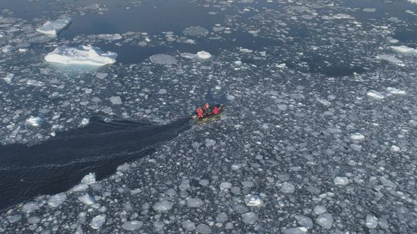 Μηχανοκίνητο σκάφος Zodiac πλέει στην Ανταρκτική πάγο. Εναέρια παρακολούθηση - μη επανδρωμένη πτήση επισκόπηση του νότιου πόλου ωκεανού τοπίο. Ελαστικό σκάφος επιπλέουν το χειμώνα ανοιχτό νερό θρυμματισμένο πάγο. - Φωτογραφία, εικόνα