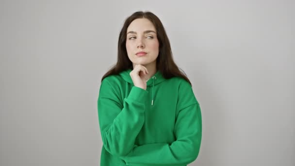 Young woman wearing sweatshirt standing with hand on chin thinking about question, pensive expression. smiling with thoughtful face. doubt concept. over isolated white background - Footage, Video