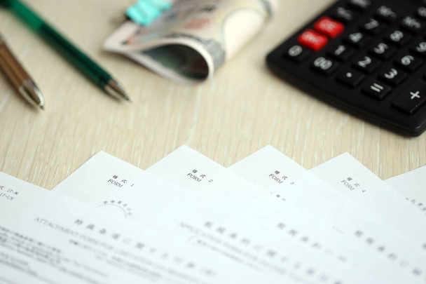 Japońskie formularze podatkowe leżą na stole z kalkulatorem, długopisem i japońskich jenów banknoty pieniężne roll up - Zdjęcie, obraz