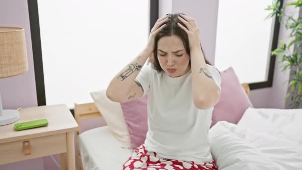 Gestresste jonge vrouw in pyjama zit op bed pijn van pijnlijke migraine. handen op het hoofd, het dragen van stress van intense hoofdpijn, lijden in haar slaapkamer. - Video