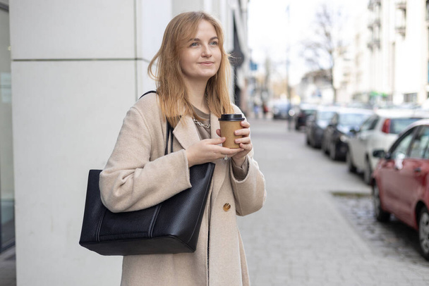 Koncepcja miejskiego stylu życia i picia. Atrakcyjna kobieta pije kawę w papierowej bio-białej filiżance. - Zdjęcie, obraz