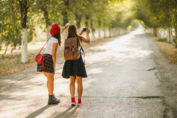 Zadní pohled na dvě mladé šťastné ženy fotí při chůzi po třídě. - Fotografie, Obrázek