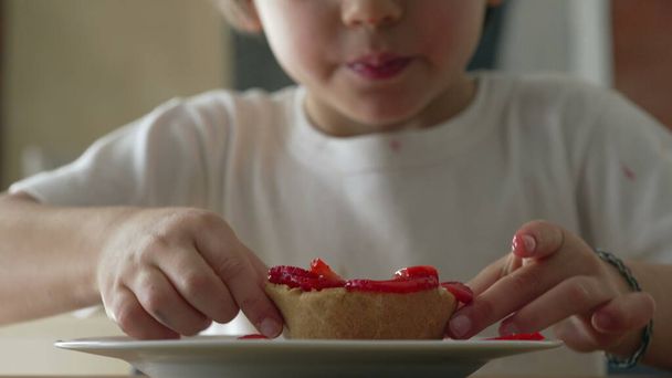 Egy kisfiú ízlelgeti a sajttorta desszertet. 5 éves gyermek ragad cukros ételt a tányérról - Fotó, kép