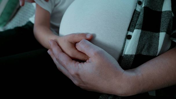 Las manos del niño y la madre abrazando el embarazo del vientre del tercer trimestre de manera tierna - Foto, Imagen