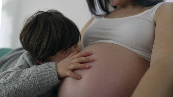 Gyengéd pillanat a kisfiúnak, amikor megérinti a terhes anya hasát, érzi a kisöccse szívverését, szimbolizálja az anyai szeretetet a késői terhességi szakaszban - Fotó, kép
