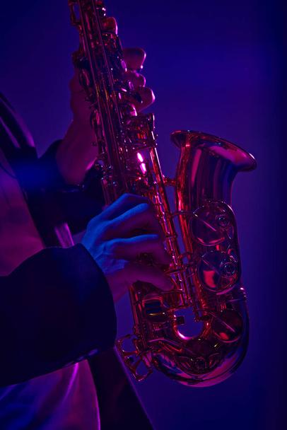 Обрізане фото талановитого сольного гравця, який виступає на саксофоні у яскравому рожевому неоновому світлі на темному студійному фоні. Концепція музики та мистецтва, хобі, концерти та фестивалі, сучасна культура. Реклама - Фото, зображення