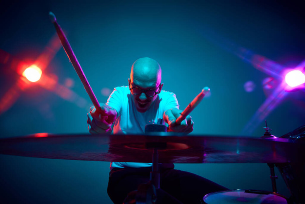 Συναισθηματικός φαλακρός ντράμερ σε casual outfit με drumsticks σε ροζ-μωβ stage lighting. Έννοια της μουσικής και της τέχνης, χόμπι, συναυλίες και φεστιβάλ, σύγχρονη κουλτούρα. ΠΑΡΑΡΤΗΜΑ II - Φωτογραφία, εικόνα