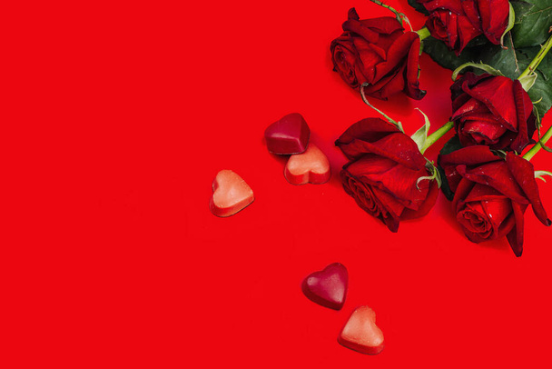 Minimalistická jarní pohlednice se sladkými čokoládovými bonbóny a růžemi. Tradiční slavnostní symbol, plochý. Vášeň červené pozadí, horní pohled - Fotografie, Obrázek
