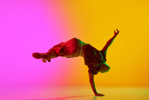 Foto dinámica de un hombre joven y talentoso bailando movimientos de estilo libre en luz de neón contra el degradado fondo rosa-amarillo. Concepto de arte, hobby, deporte, creatividad, moda y estilo, acción. Anuncio - Foto, imagen