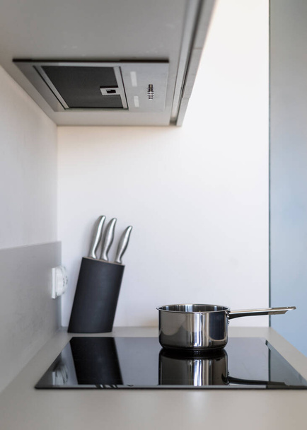 Σύγχρονη κουζίνα απορροφητήρα κουκούλα πάνω από χτισμένο ηλεκτρικές εστίες με κατσαρόλα. Γυάλινη κεραμική επαγωγική σόμπα κοντά στο σύνολο των μαχαιριών στη βάση για την κοπή τροφίμων, κάθετη βολή - Φωτογραφία, εικόνα