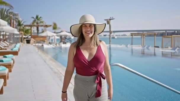 Mosolygó nő sunhat áll egy luxus medence mellett trópusi tenyérrel egy üdülőhelyen - Felvétel, videó