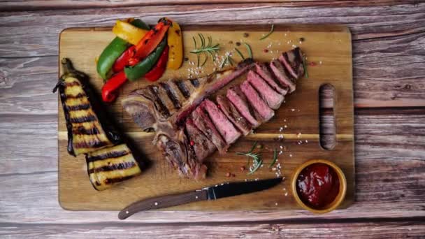 T-bone hovězí steak grilovaný na dřevěné desce s grilovanou zeleninou. Horní pohled - Záběry, video