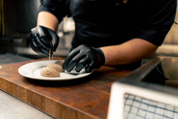 close-up in een professionele keuken chef-kok in zwarte handschoenen inserts tandenstokers in een delicatesse - Foto, afbeelding