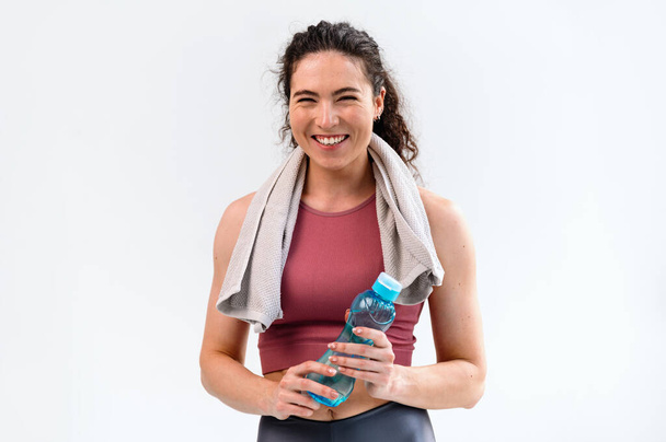 Cintura hacia arriba retrato de sonriente entrenadora de fitness femenina feliz mirando a la cámara y sosteniendo la botella con agua. Motivación para un concepto de estilo de vida saludable. Copiar espacio. - Foto, Imagen