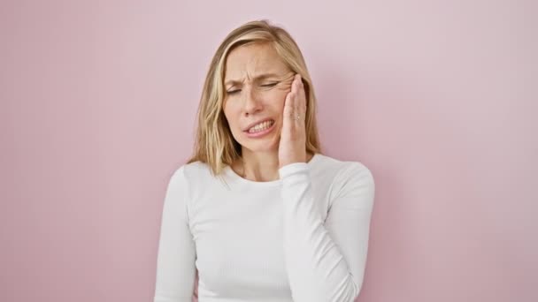 Blond jongedame grijpen mond in pijn - pijnlijke uitdrukking van kiespijn, tandheelkundige ziekte duidelijk. geïsoleerd op roze, wachten tandartsen zorg  - Video