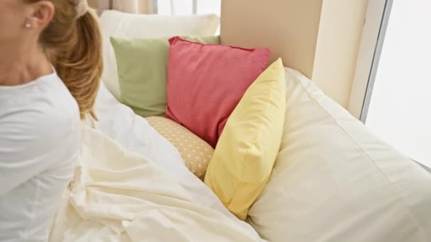 Dojrzała kobieta odpoczywa w jasnej sypialni z kolorowymi poduszkami, przedstawiając relaks i komfort w domu. - Materiał filmowy, wideo