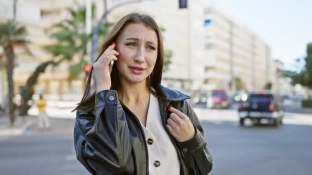 Preocupada morena jovem fala ao telefone em uma rua movimentada da cidade - Filmagem, Vídeo