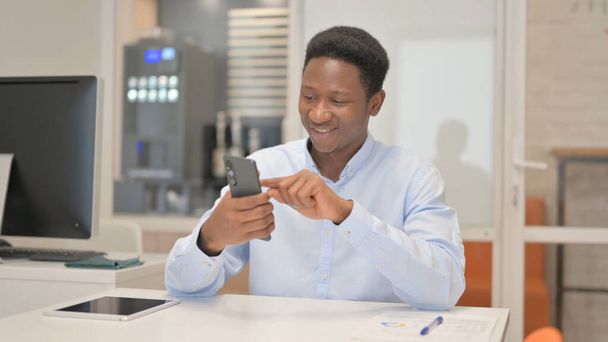 Afrikanischer Geschäftsmann surft im Büro am Telefon im Internet - Foto, Bild