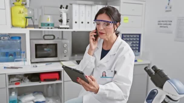 Ammattimainen naistutkija laboratoriossa, jossa on digitaalinen tabletti ja puhelu. - Materiaali, video