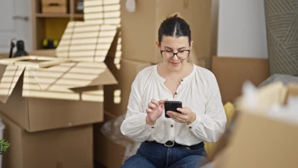 Giovane bella donna ispanica utilizzando smartphone seduto sul divano a nuova casa - Filmati, video
