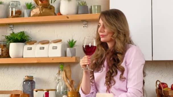 Mujer bebiendo una copa de vino tinto y bailando en la cocina - Imágenes, Vídeo