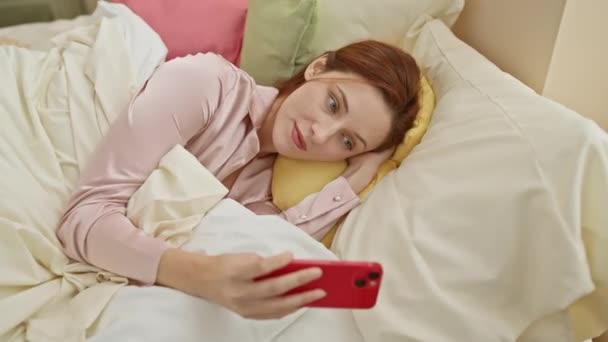Rahat bir kadın akıllı telefonuyla yatakta uzanıyor, rahatlığı, rahatlığı, teknolojiyi ve ev yaşamını somutlaştırıyor.. - Video, Çekim