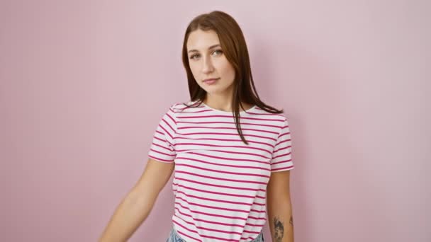 Cheerful young brunette, sporting a striped tshirt, playfully covering her eyes with hand for a blind surprise, over a pink isolated background. - Footage, Video