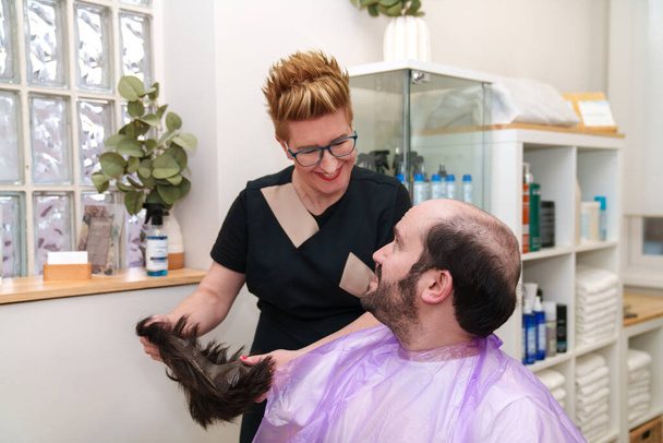 Estilista se ríe con el cliente mientras que la eliminación de la peluca para el mantenimiento. - Foto, imagen