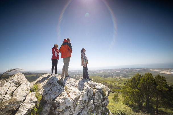 Een groep vrienden staat op een grote rotsformatie, kijkend naar het landschap. Ze genieten van het uitzicht en maken foto 's van het landschap. - Foto, afbeelding