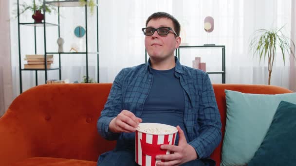 Běloch v 3D brýle sedí na gauči jíst popcorn občerstvení a sledovat zajímavé televizní seriál sportovní hra, film on-line sociální média filmový obsah doma byt. Chlap si užívá zábavu. - Záběry, video