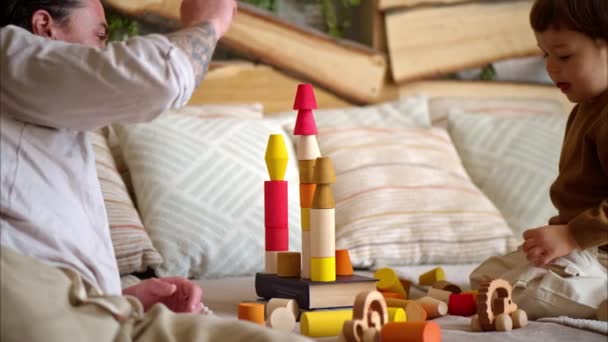 Батько грає зі своїм сином з барвистими, екологічними дерев'яними іграшками на ліжку - Кадри, відео
